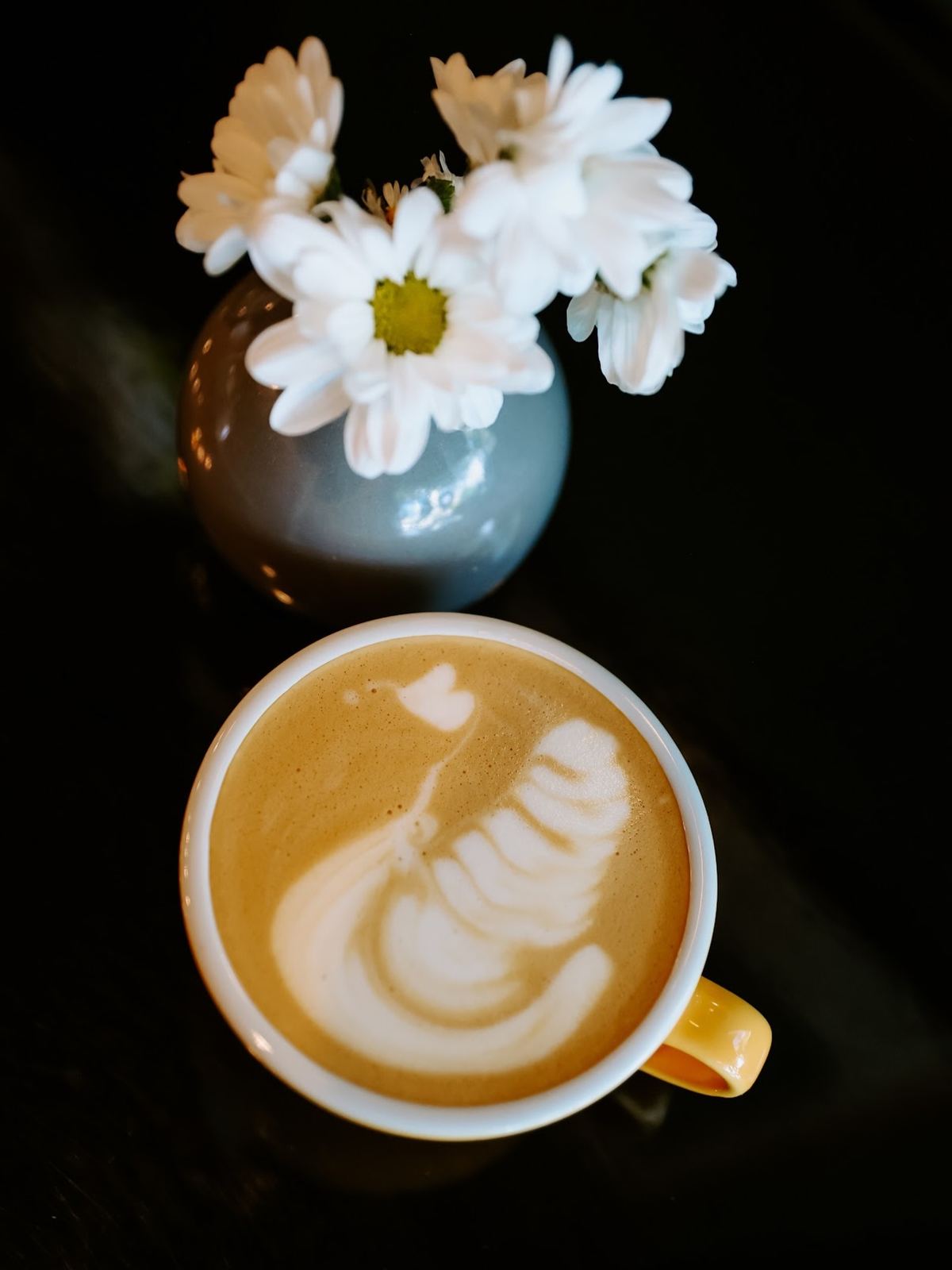 Latte cu latte art lângă o vază cu margarete